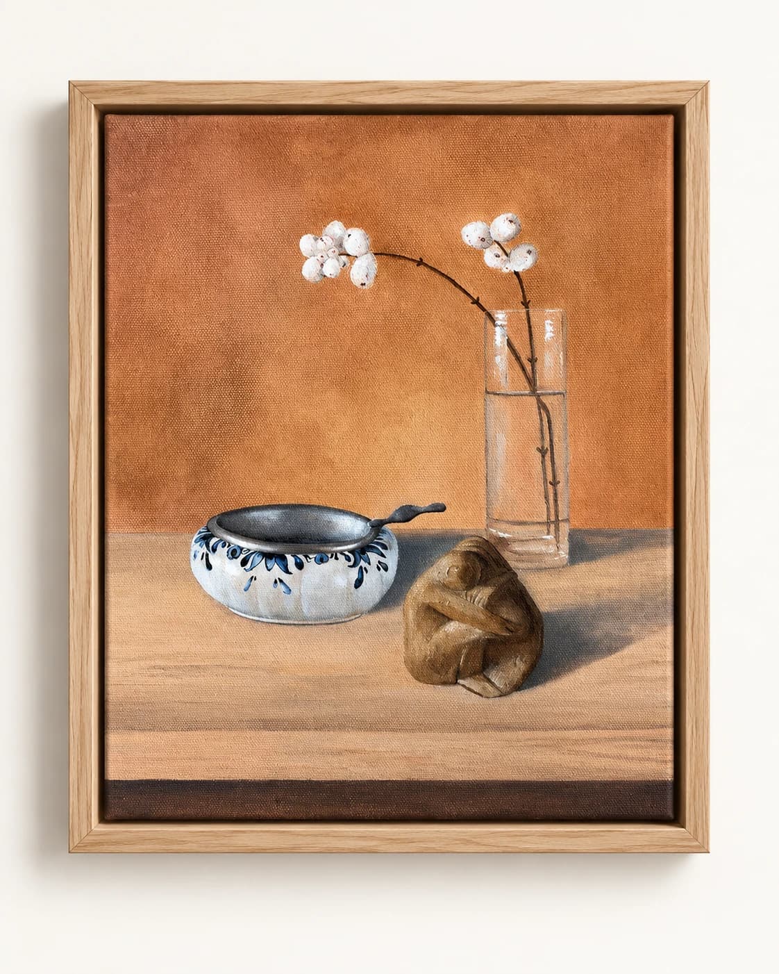 Een kom, een glazen vaas met bloemen en een klein voorwerp op een tafel, in een houten lijst.