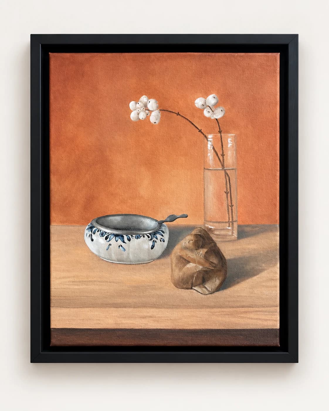 Een kom, een glazen vaas met bloemen en een klein voorwerp op een tafel, in een zwarte lijst.